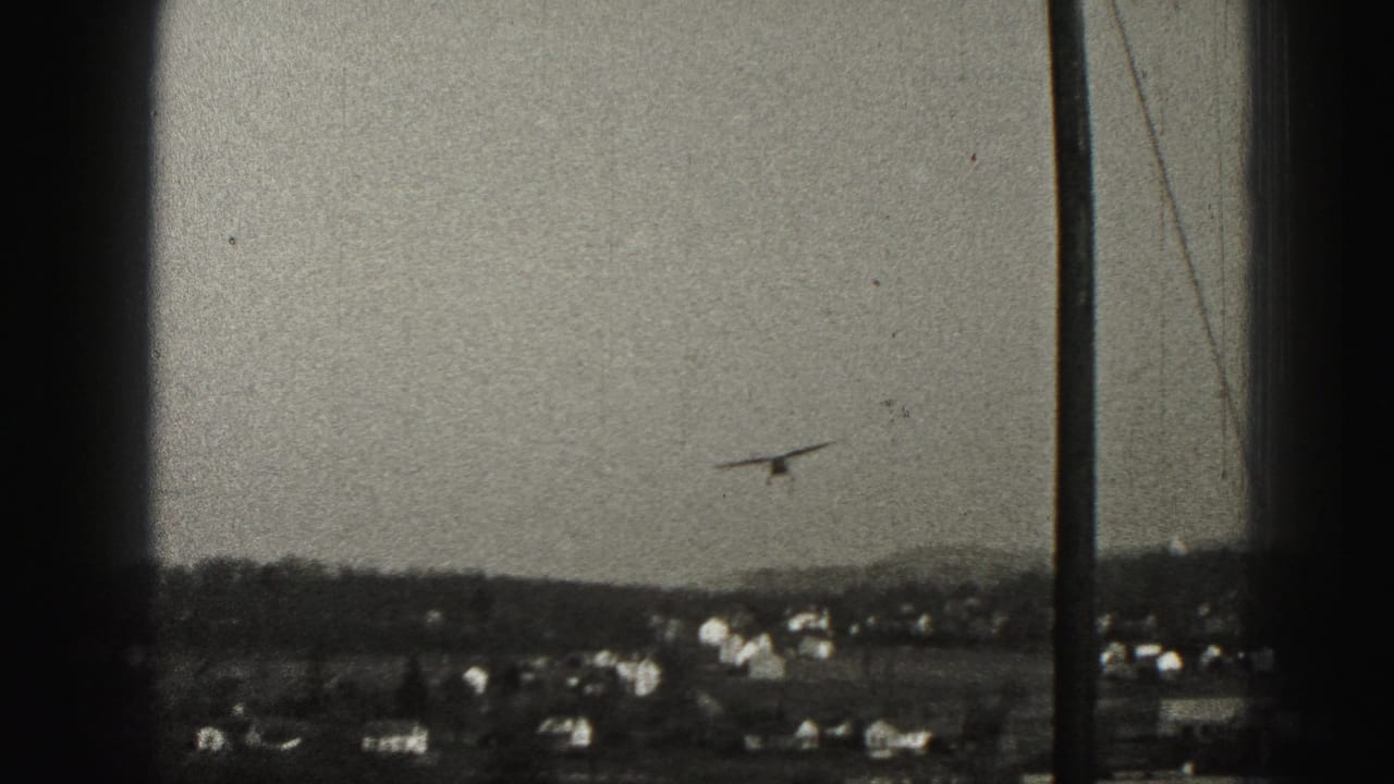 A small plane flies low over a Harrisburg-area suburban horizon, seen through dark window-like framing.