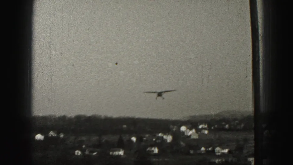The small aircraft is centered above rooftops and hills in grainy 1975 Harrisburg-area 8mm footage.