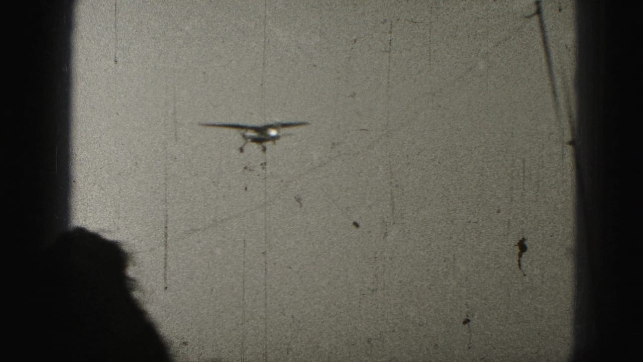 Small aircraft in flight over Harrisburg, Pennsylvania, in 1975 home-movie footage, with visible 8mm scratches and dark gate edges.