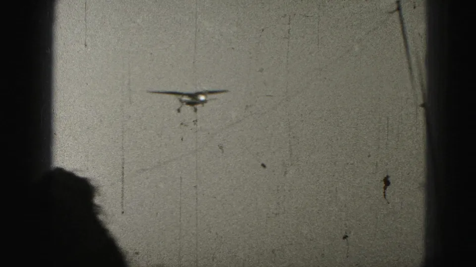 Small aircraft in flight over Harrisburg, Pennsylvania, in 1975 home-movie footage, with visible 8mm scratches and dark gate edges.