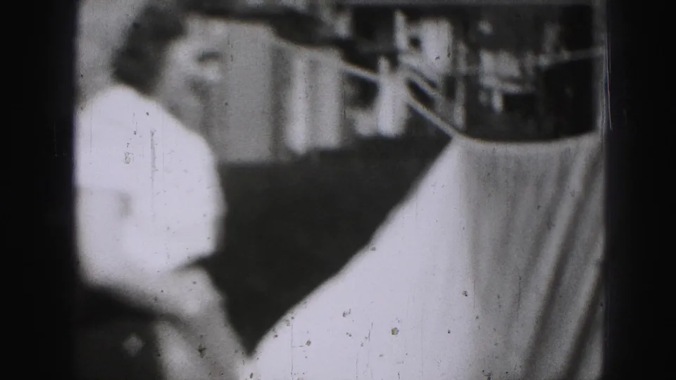 In Harrisburg 1975 home-movie footage, a woman stands near a clothesline while a large sheet fills the foreground.