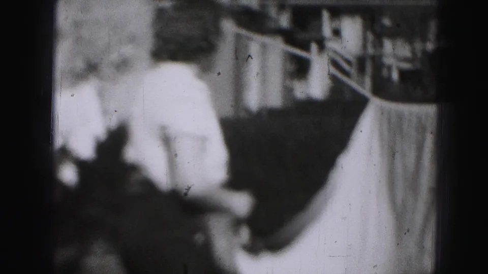 The woman turns away from the camera near a bright sheet on a backyard clothesline in 1975 Harrisburg footage.