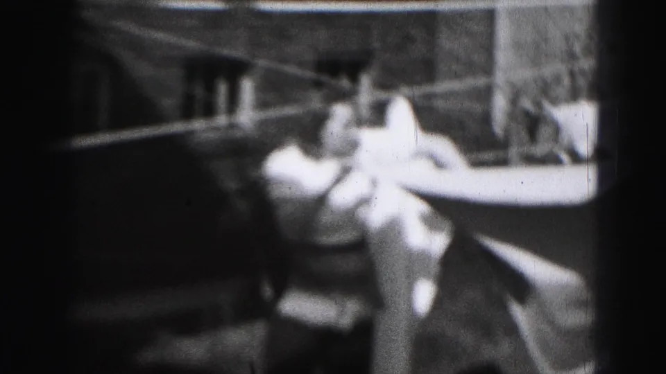1975 Harrisburg home-movie frame of a woman handling light laundry on an outdoor clothesline.