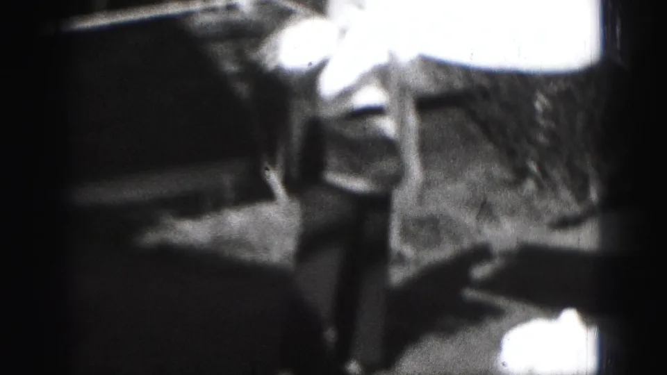 Grainy 1975 Harrisburg 8mm frame showing a woman beside a clothesline with bright laundry overhead.