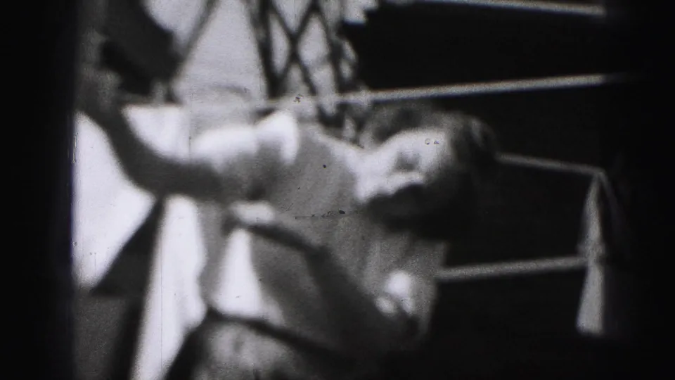 A close 8mm frame shows the woman pinning a white garment to a backyard clothesline in Harrisburg, Pennsylvania.