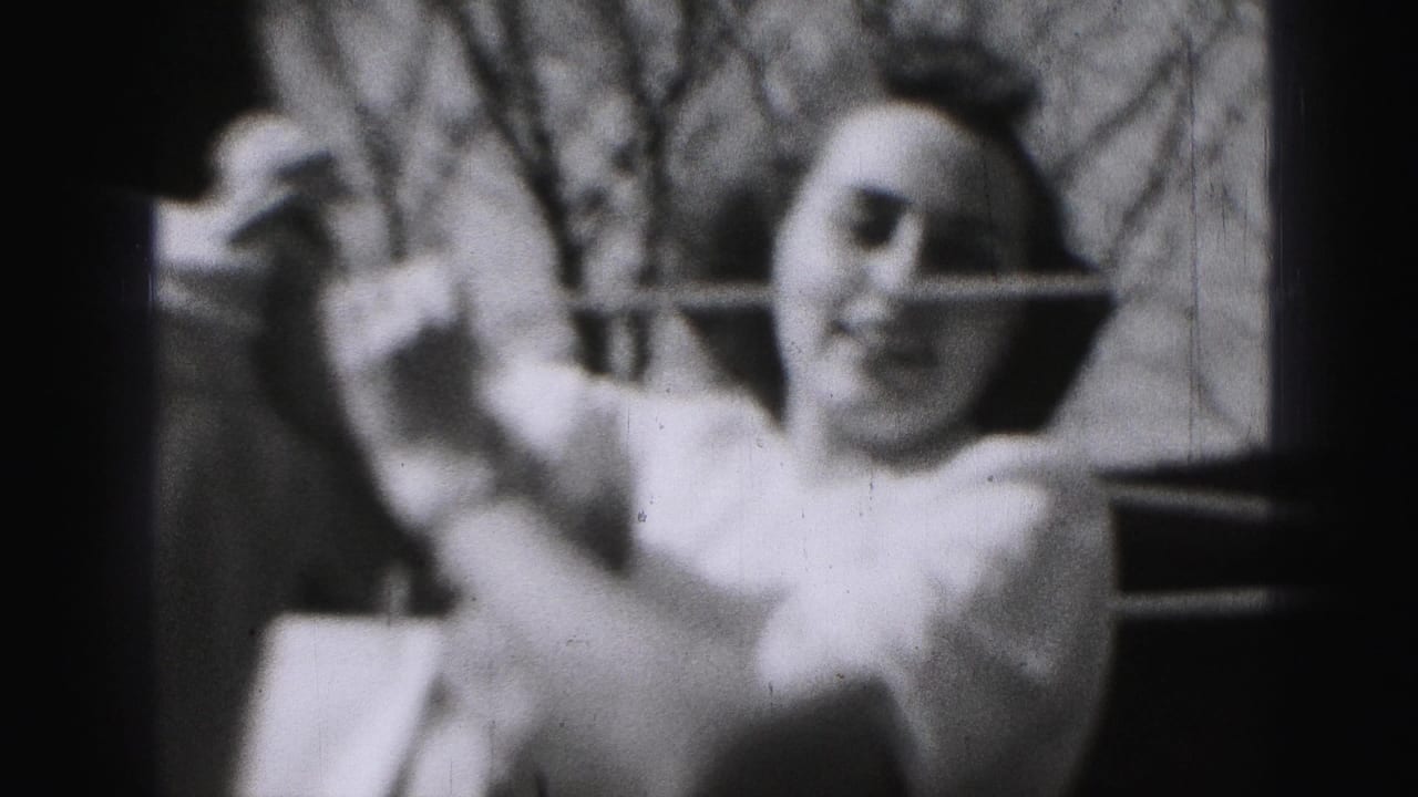 In 1975 Harrisburg home-movie footage, a woman in a light shirt reaches toward a backyard clothesline with bare trees behind her.