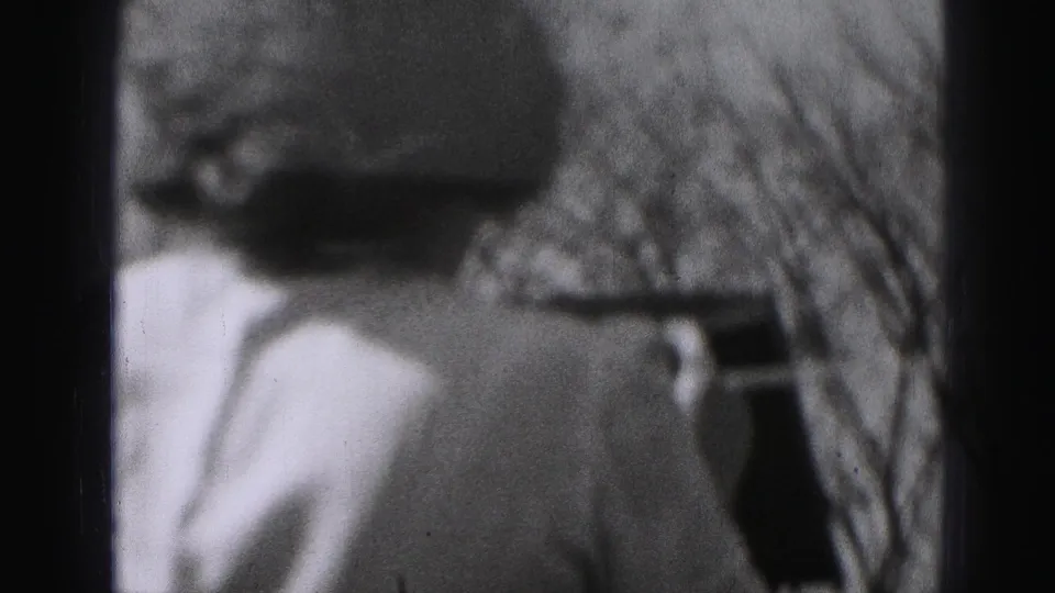 A soft side view shows the woman beside the clothesline, with bare branches and backyard structures in the 8mm frame.