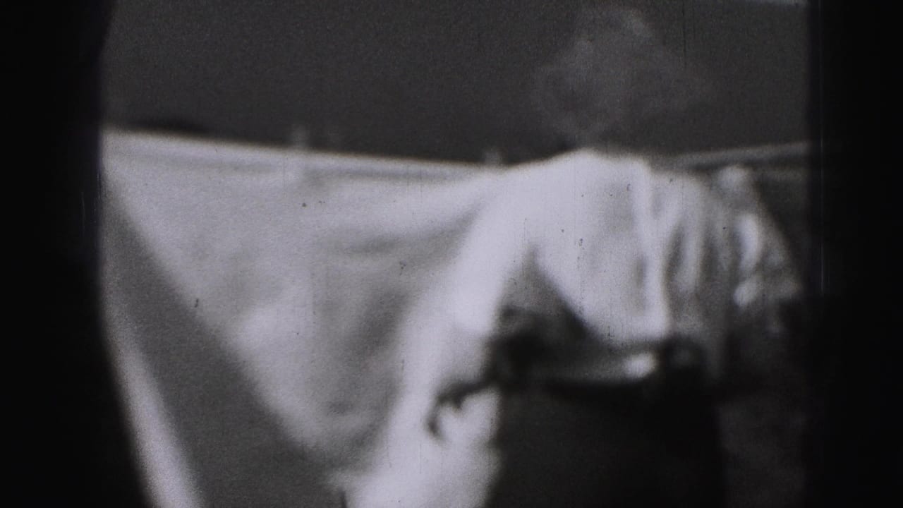 A white sheet fills most of the frame on a backyard clothesline, with the woman partly visible at right in the 1975 Harrisburg footage.