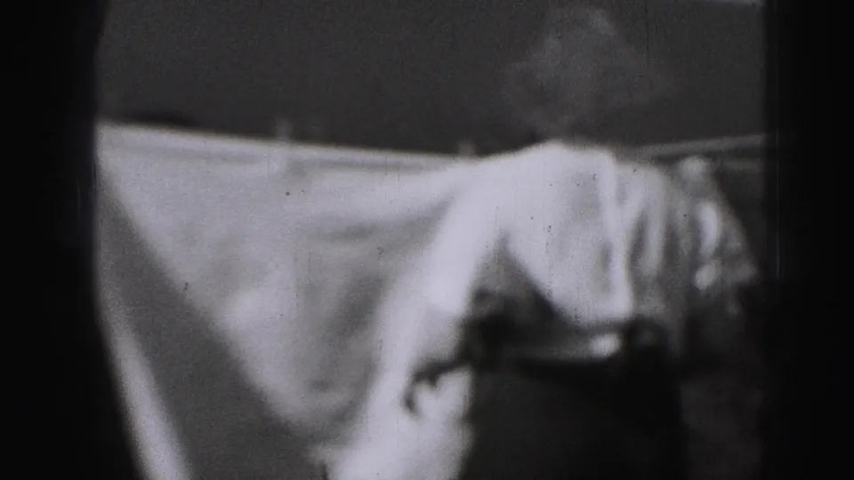 A white sheet fills most of the frame on a backyard clothesline, with the woman partly visible at right in the 1975 Harrisburg footage.