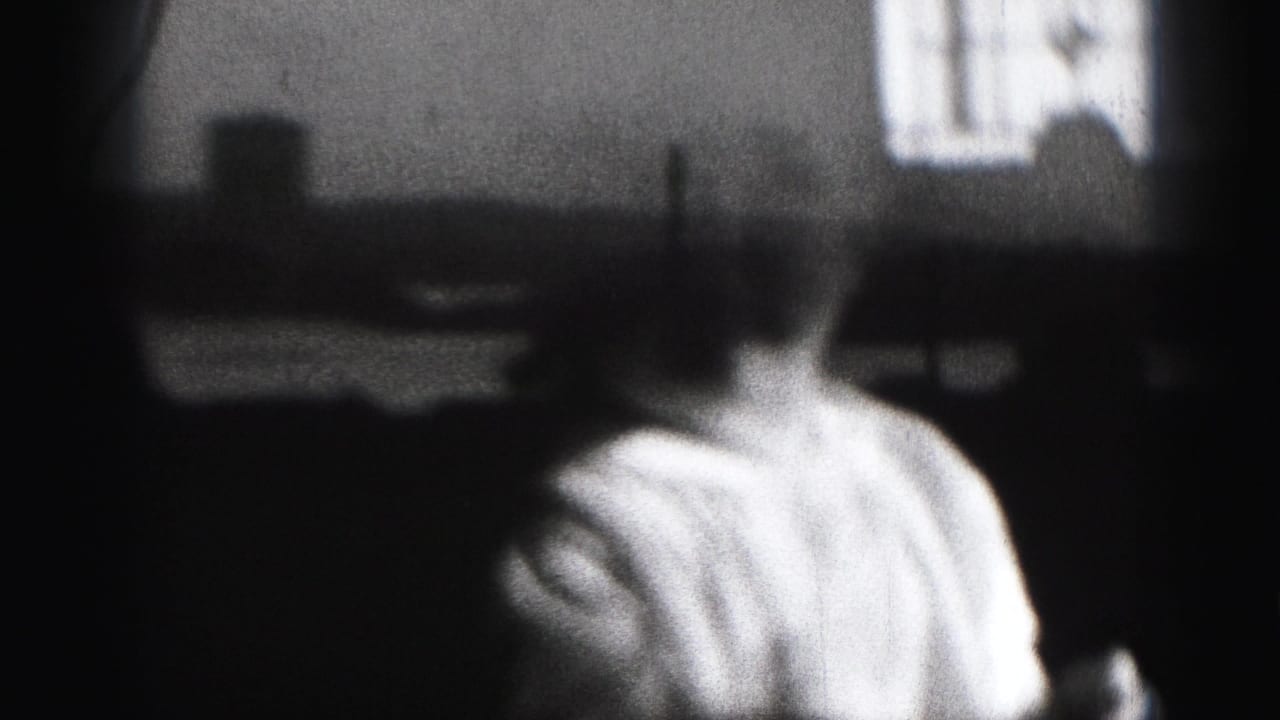 1975 8mm home-movie frame from Harrisburg showing a baby in a light outfit, softly focused against a bright interior window or screen.