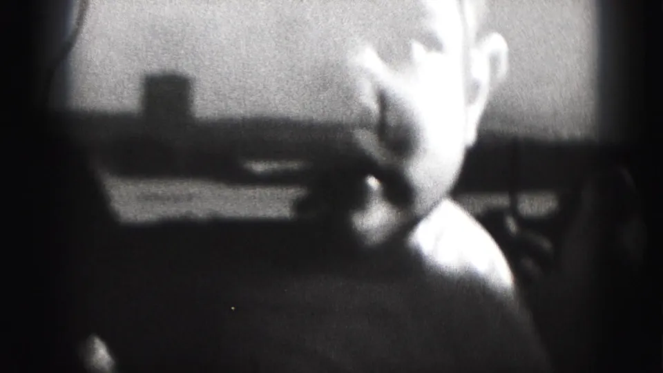 Soft-focus 1975 8mm frame of the baby in side view inside a dim Harrisburg room, with strong backlight and visible film grain.