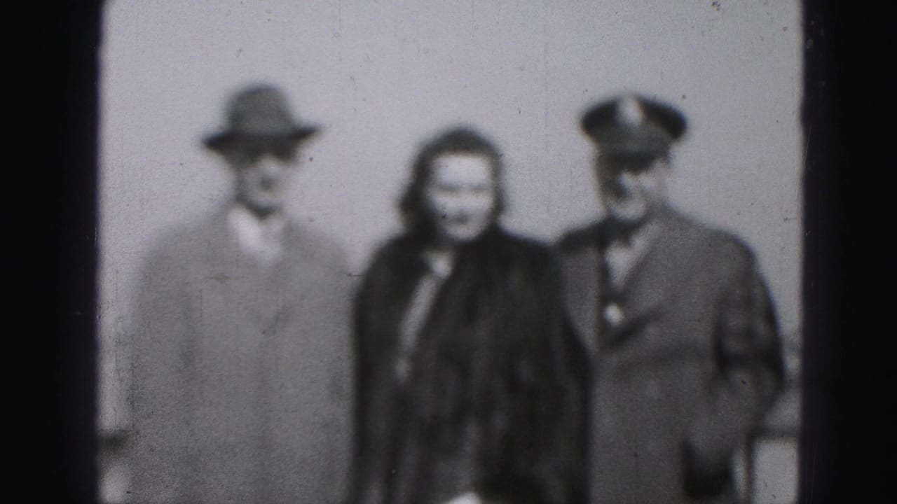 Soft black-and-white 8mm frame from Harrisburg, Pennsylvania, showing a woman in a dark fur coat between a hatted man and a uniformed man.