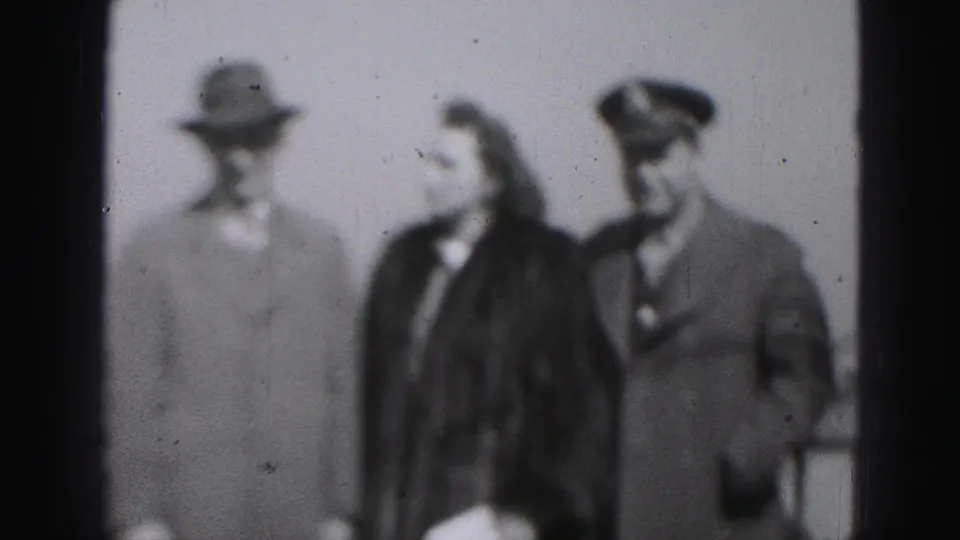 Three adults in formal coats and hats appear together in Harrisburg, Pennsylvania, in a soft 1975 8mm black-and-white frame.
