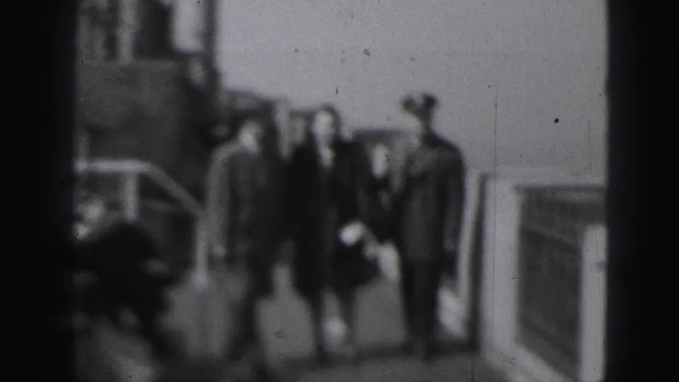 A wider 1975 Harrisburg home-movie view shows the three adults on a public walkway near a railing and background structure.