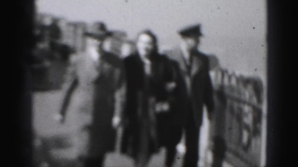 The woman and two men continue toward the camera in the 1975 8mm scene, framed by the ship deck railing and blurred figures behind them.