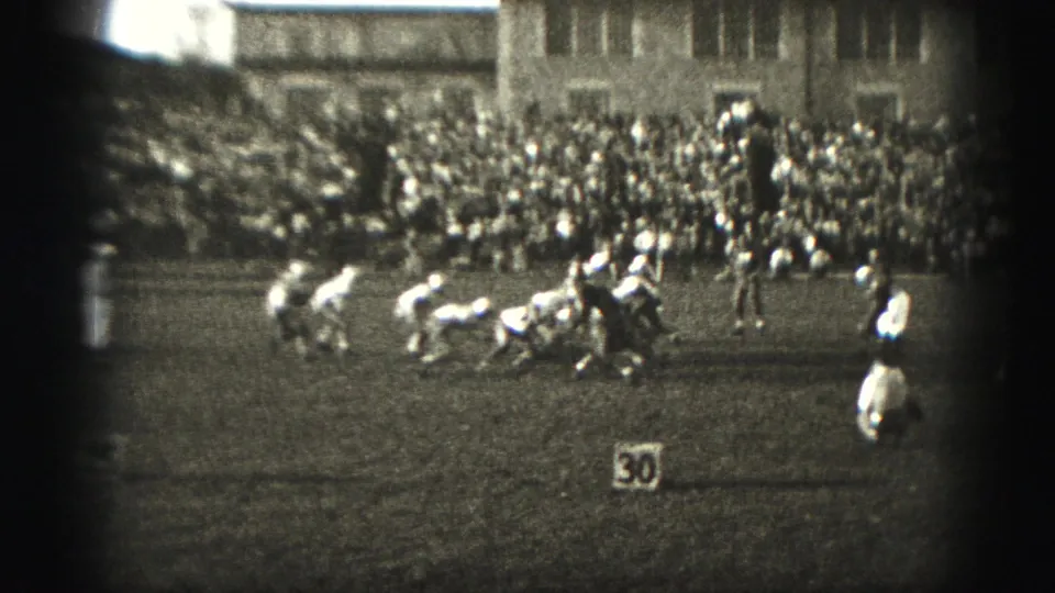 1975 Harrisburg high school football players appear set at the line of scrimmage as spectators fill bleachers behind them.