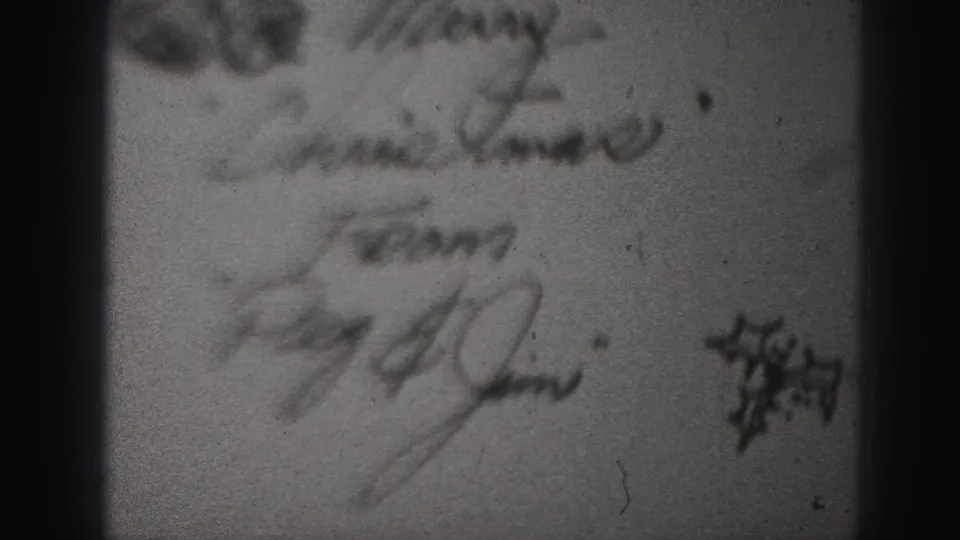 Soft 8mm frame from a Harrisburg 1975 home movie showing a blurred handwritten Christmas note signed Peg and Jim.