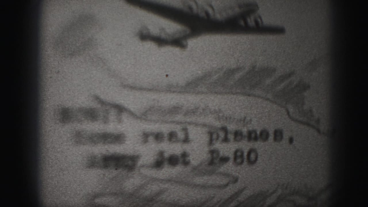 1975 8mm frame from Harrisburg showing a soft, grainy filmed photograph of an airplane with partially readable text referencing an Army Jet P-80.