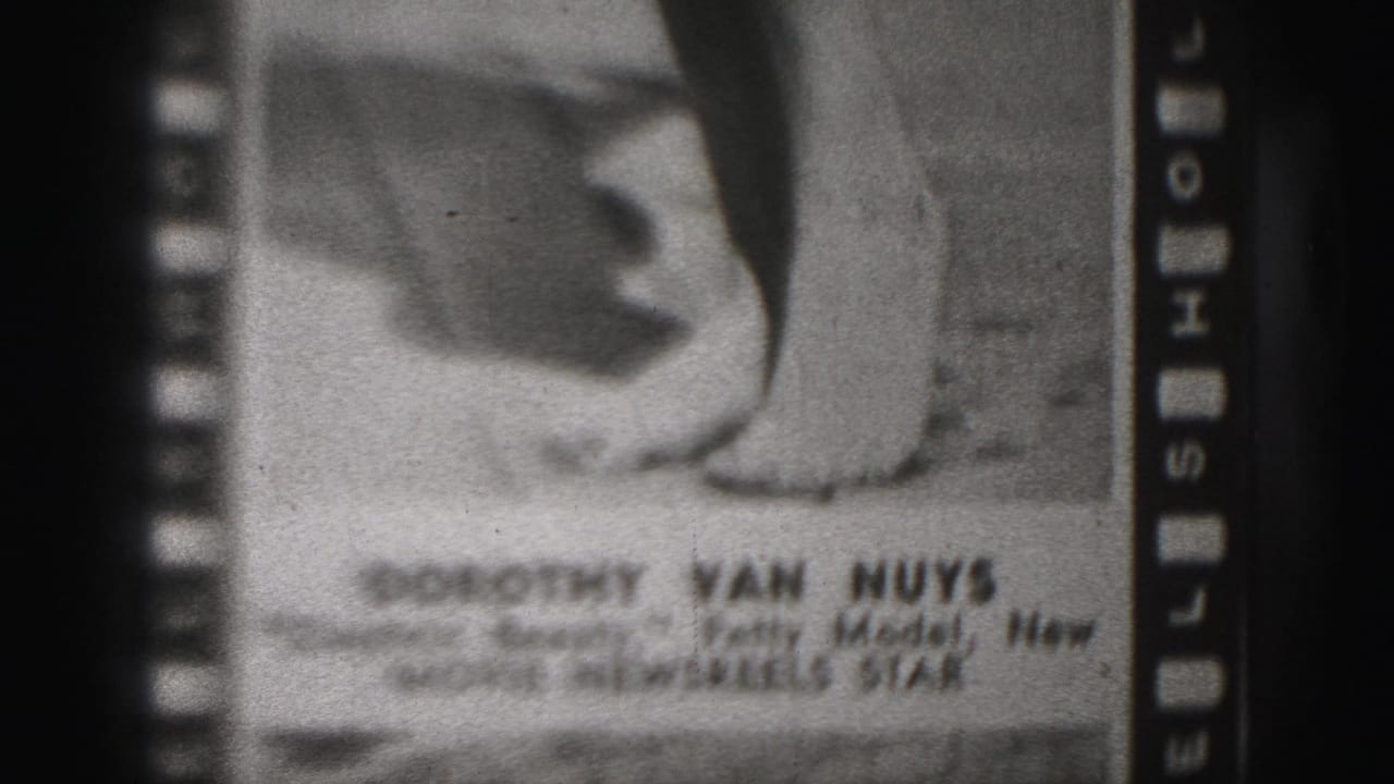 1975 8mm frame showing a filmed photograph labeled with Dorothy Van Nuys and Movie Newsreel Star text, with a hand and lower body visible.