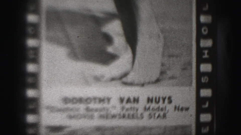 1975 8mm frame showing a filmed photograph labeled with Dorothy Van Nuys and Movie Newsreel Star text, with a hand and lower body visible.