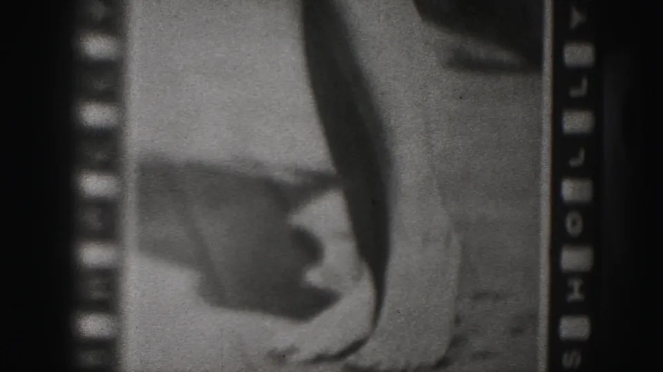 1975 8mm frame from Harrisburg with sprocket holes beside a blurred photographed figure, showing legs and a hand near the lower edge.