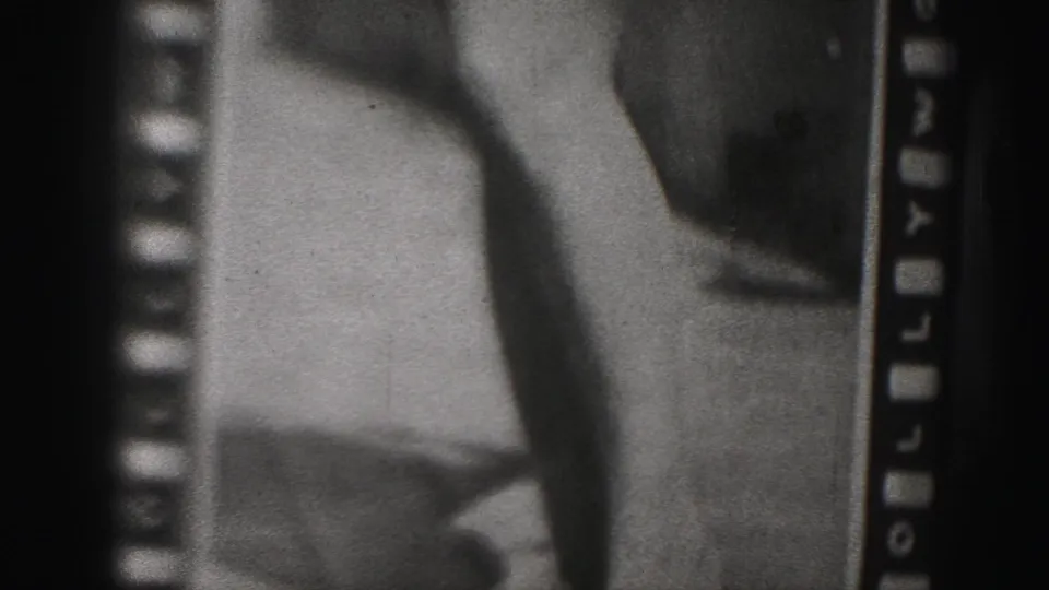 1975 8mm frame showing a soft, grainy close-up of a photographed person's lower body, with sprocket holes and dark film borders visible.