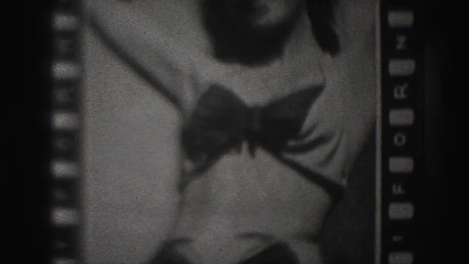 1975 Harrisburg home-movie frame showing a close cropped woman in a dark bikini, with sprocket holes and film edge visible.