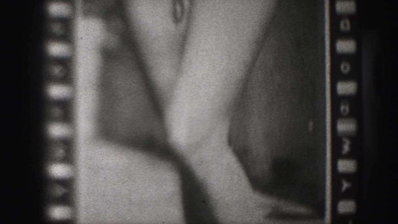 Soft black-and-white frame showing a poster detail of bare legs and feet beside sprocket edges.