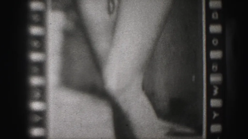 1975 Harrisburg 8mm frame showing a close poster detail with bare legs, feet, film grain, and sprocket borders.