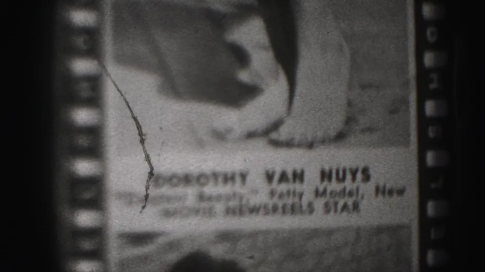 1975 Harrisburg 8mm frame showing a poster close-up with bare feet, sprocket borders, scratches, and Dorothy Van Nuys text.