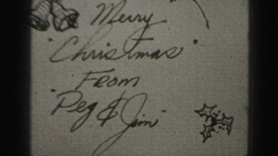 Close-up of a handwritten Christmas greeting reading in part Merry Christmas from Peg and Jim, with small holly sketches on film.