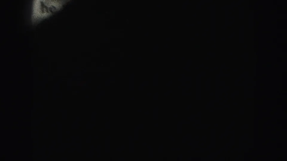 A near-black transition frame from the 8mm scan, with a narrow partial edge of paper barely visible at left.