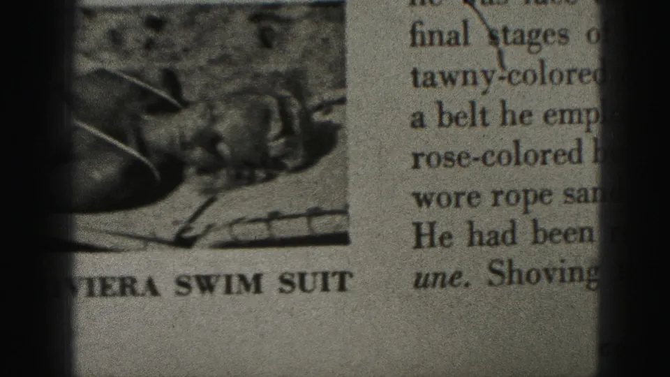 1975 Harrisburg 8mm frame showing a close-up of a printed page with a cropped swimsuit model photograph and partial bold caption text.