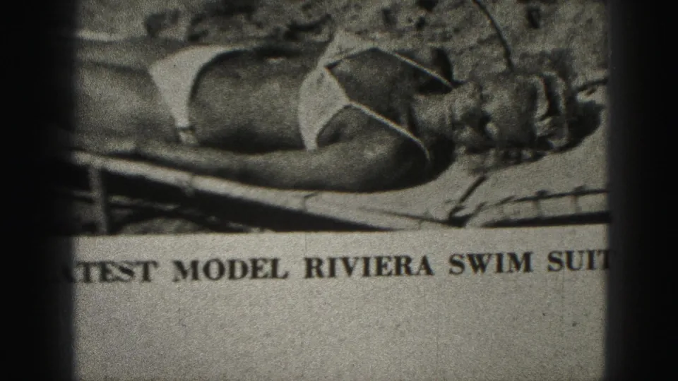 1975 Harrisburg 8mm frame showing the lower part of a printed swimwear page, with a model on a lounge chair and partially cropped caption.