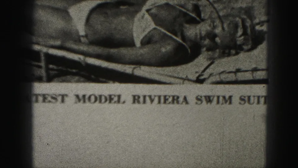 1975 Harrisburg 8mm frame showing a close-up of a printed swimsuit model photograph with partially readable bold Riviera swim suit text.