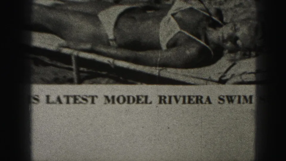 1975 Harrisburg 8mm frame showing part of a printed bikini advertisement with a reclining model, lounge chair, bold caption text, grain, and dark borders.