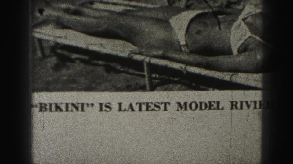 1975 Harrisburg 8mm frame of a printed swimsuit advertisement, with the bikini model partly cropped and bold text reading in part “BIKINI” and “LATEST MODEL.”