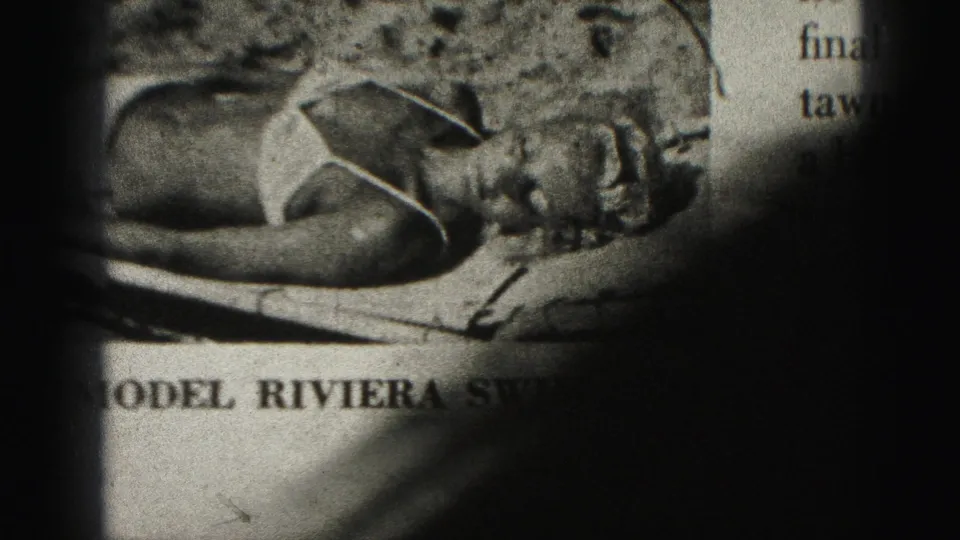 1975 Harrisburg 8mm frame of the printed Riviera swimsuit advertisement, with the model, caption text, and page partly hidden by dark film-gate shadow.