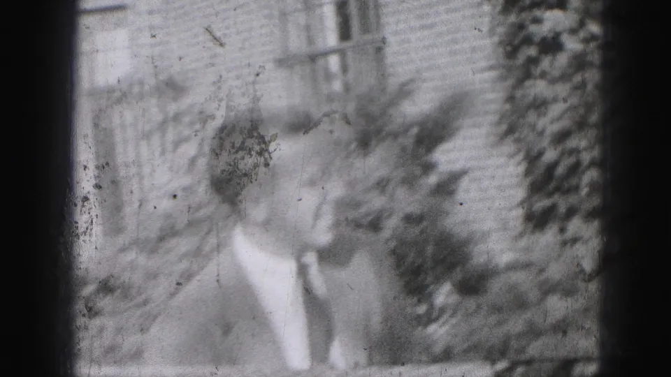 A suited adult man stands outdoors in Harrisburg, Pennsylvania, in 1975, with brickwork and foliage behind him.