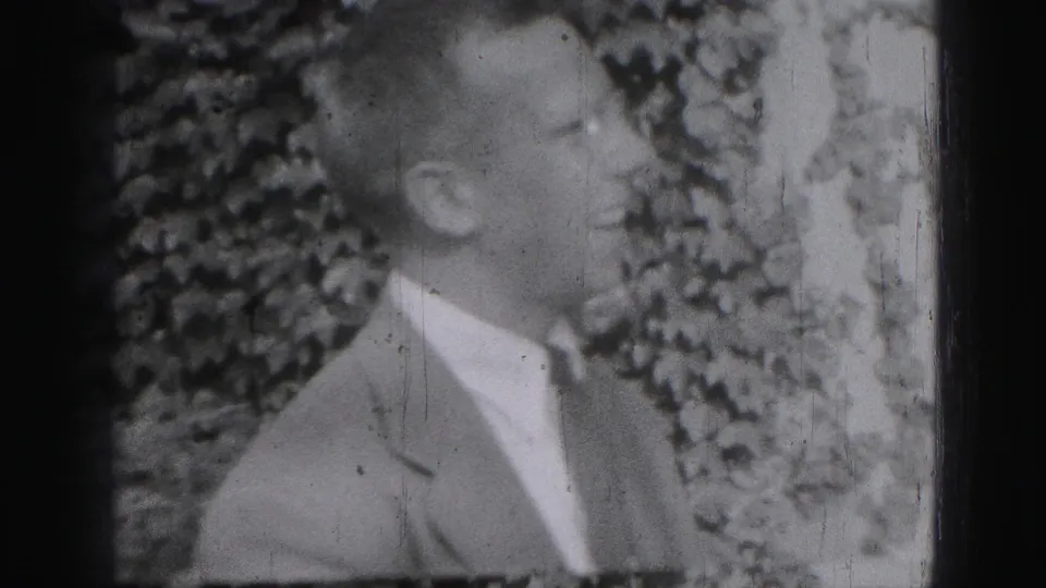 A suited adult man looks upward or toward someone off frame in the Harrisburg home-movie footage.