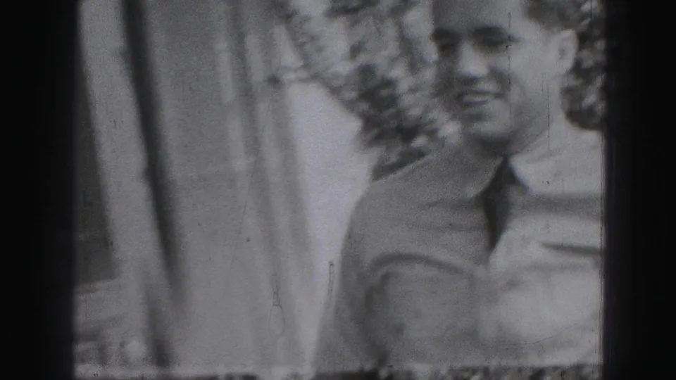 In this 1975 Harrisburg home-movie frame, a man in a light shirt and tie appears close to the camera near a residential wall.