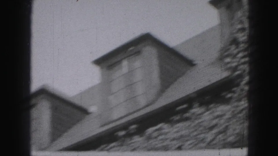 Black-and-white 8mm frame showing dormer windows and roof edges on an older Harrisburg building exterior.