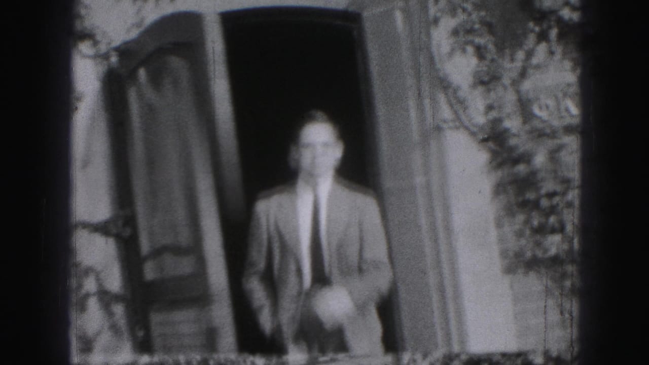 Adult man in a suit and tie appears in a doorway, smiling toward the camera in black-and-white 8mm footage.