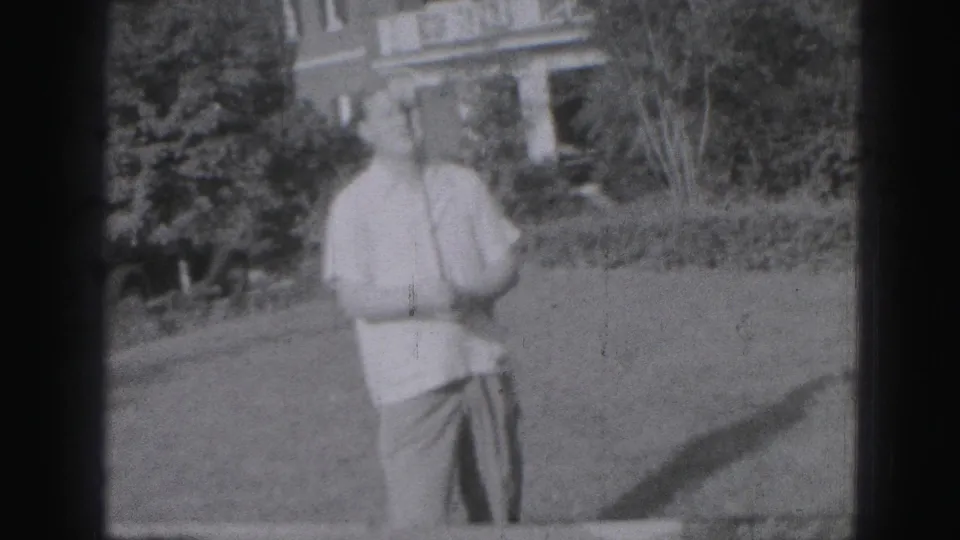 Adult man in casual clothing stands on a lawn near shrubs and a house exterior in the supplied Harrisburg 1975 context.