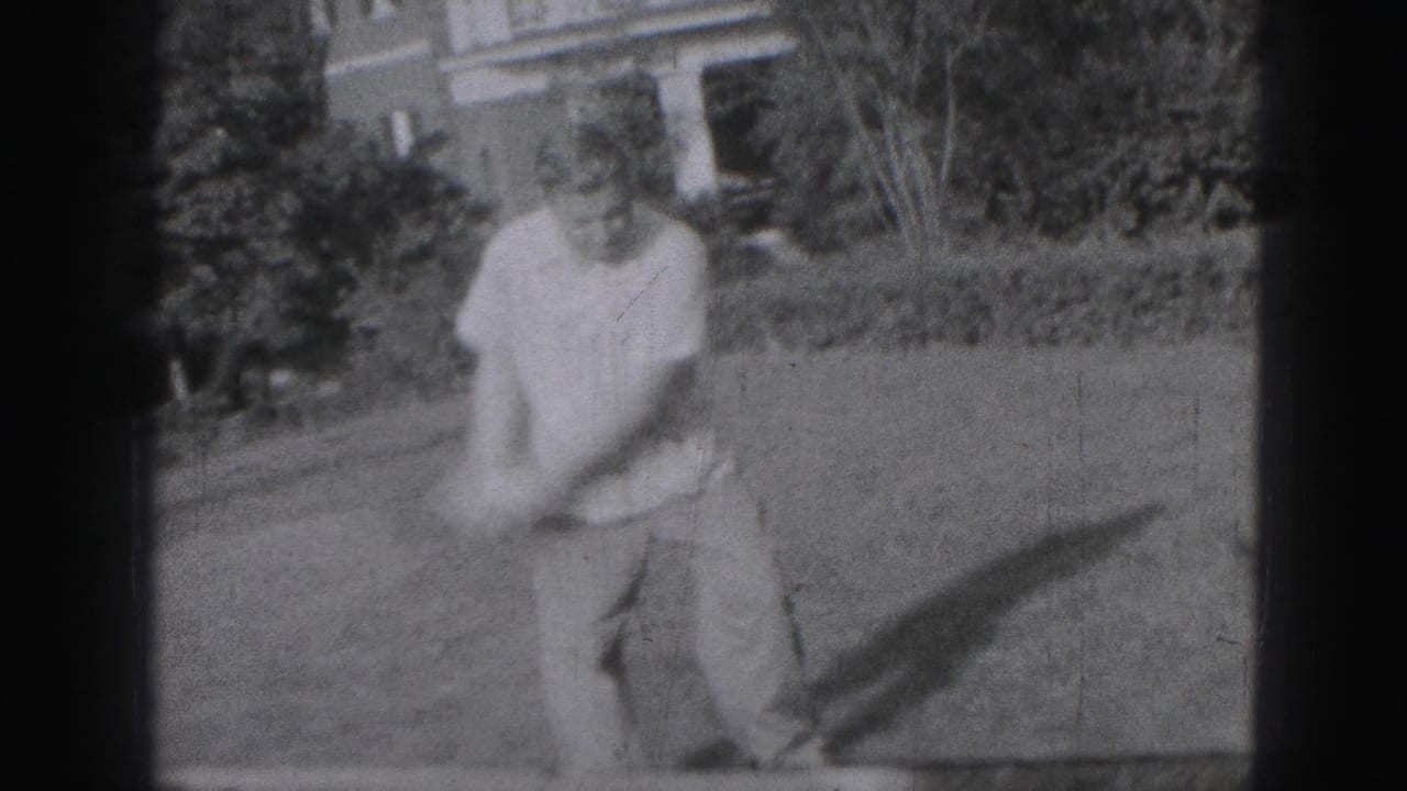 In 1975 Harrisburg home-movie footage, a man swings a golf club across a grassy yard with his shadow stretching to the side.