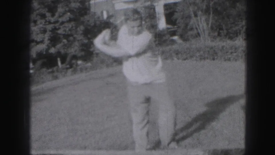 Adult man in light clothing stands with a golf club on a Harrisburg lawn in 1975 home-movie footage.