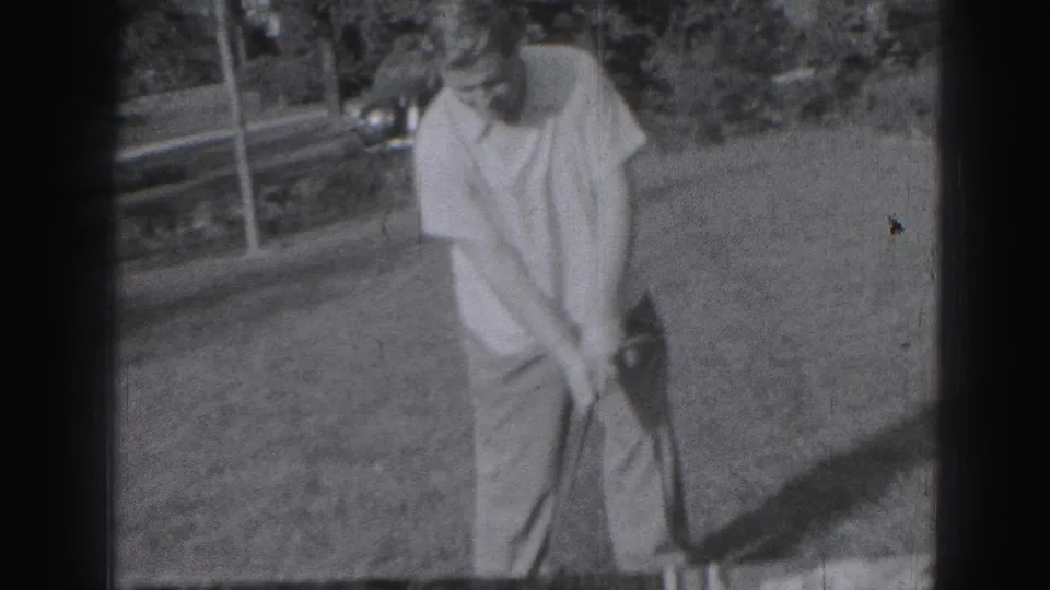 Adult man in light clothing addresses or swings at a golf ball on a Harrisburg lawn in 1975 footage.