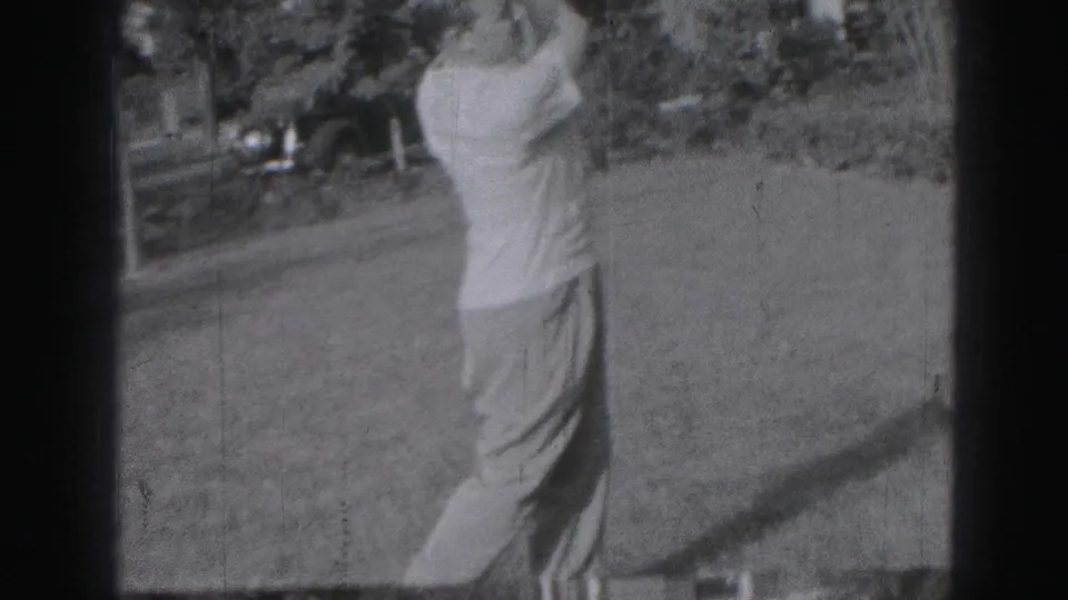 Adult man completes a golf swing on a Harrisburg lawn, captured in soft 1975 8mm home-movie footage.