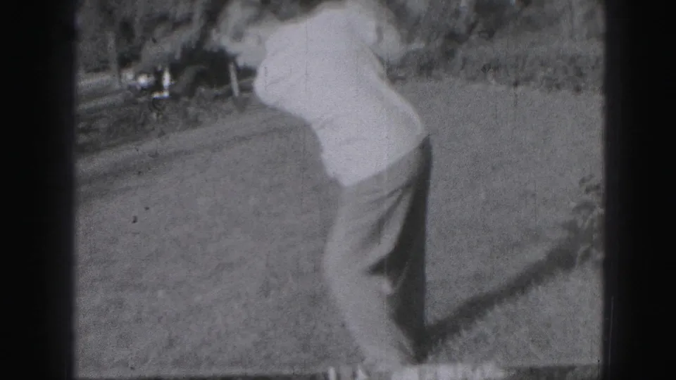 The golfer turns away from the camera during a swing on the grassy lawn, with the handheld 8mm frame showing soft focus and gate edges.