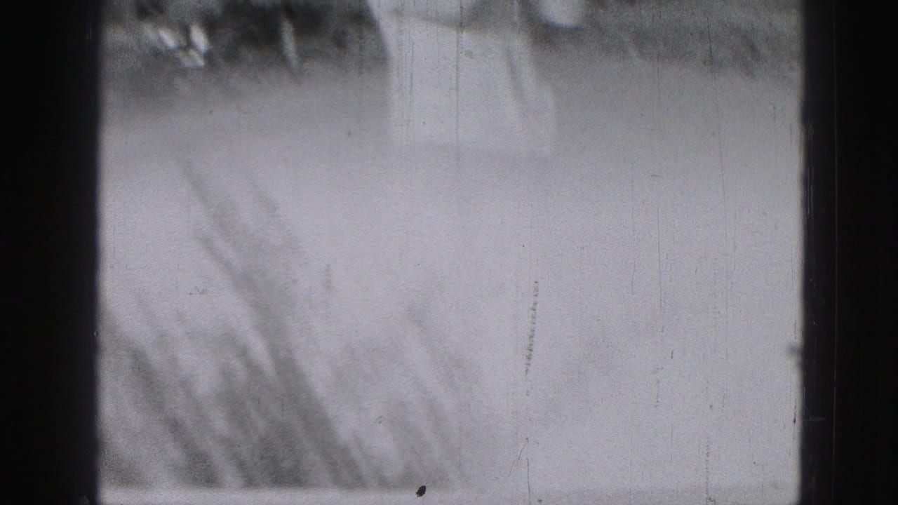 Soft black-and-white 8mm frame with heavy exposure and film-edge marks before the golf action is clearly visible.